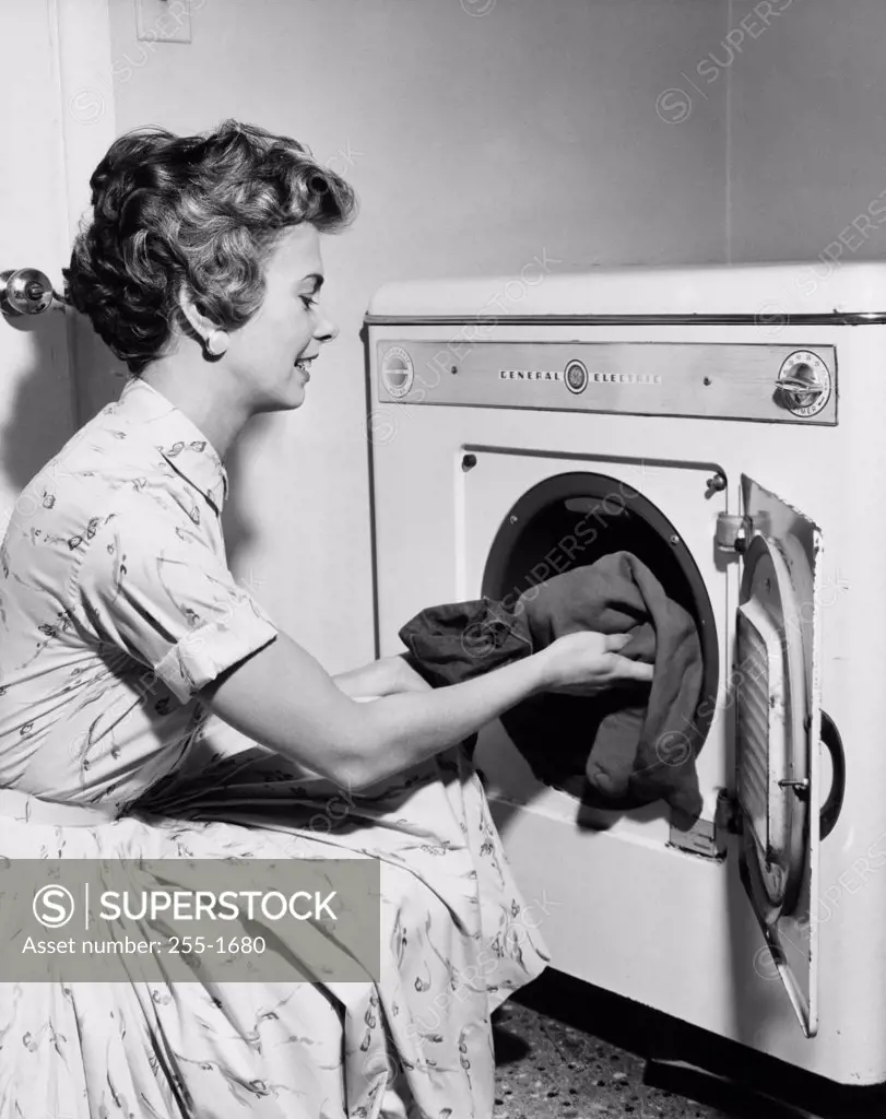 Side profile of a young woman putting clothes in the dryer