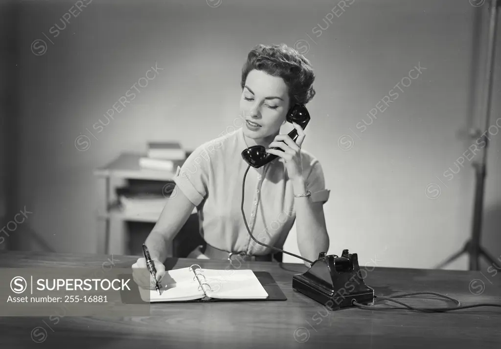 Vintage photograph. Woman at desk with notebook talking on phone.