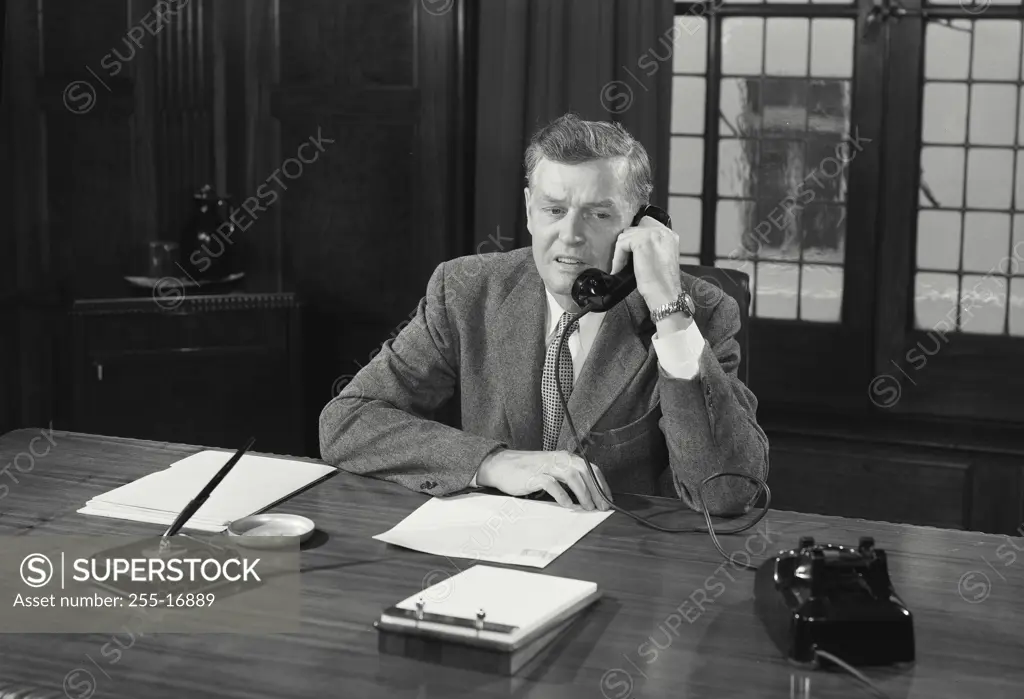 Vintage Photograph. Man in suit sitting at desk talking on telephone. Frame 4