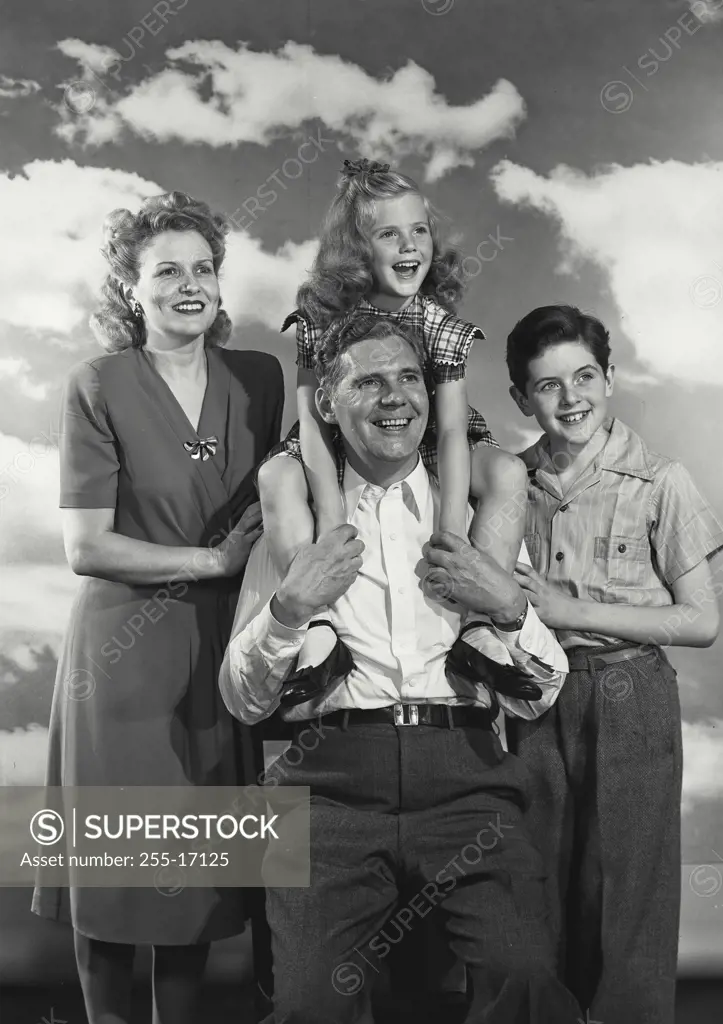 Vintage Photograph. Dressed up family of Father, Mother, son and daughter smiling with young daughter sitting on father's shoulders