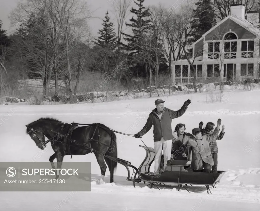 Mature couple with their children riding in a horsedrawn sleigh and waving their hands