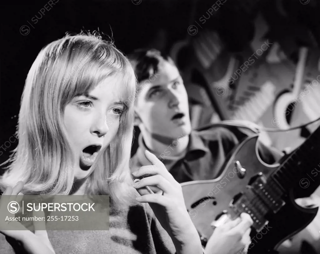 Young woman singing with electric guitarist playing guitar in background
