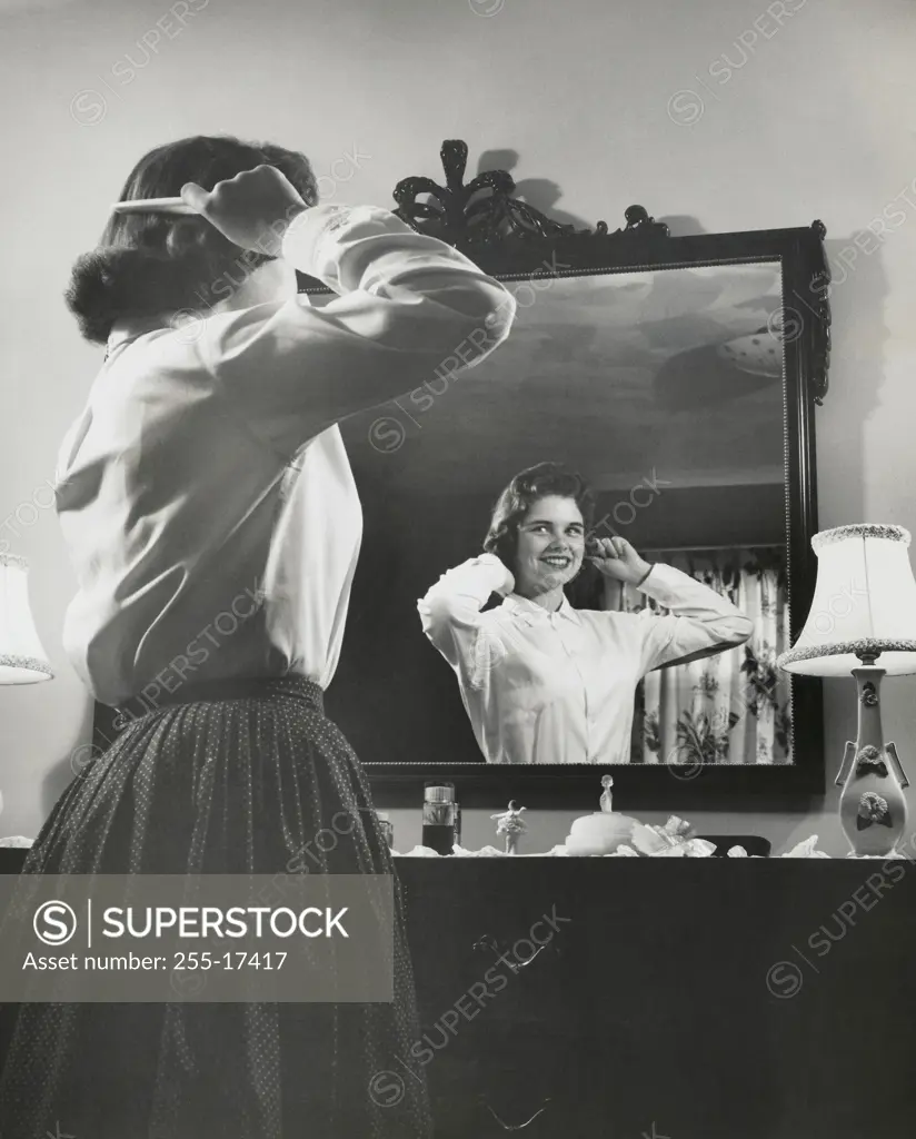 Side profile of a teenage girl combing her hair in front of a mirror