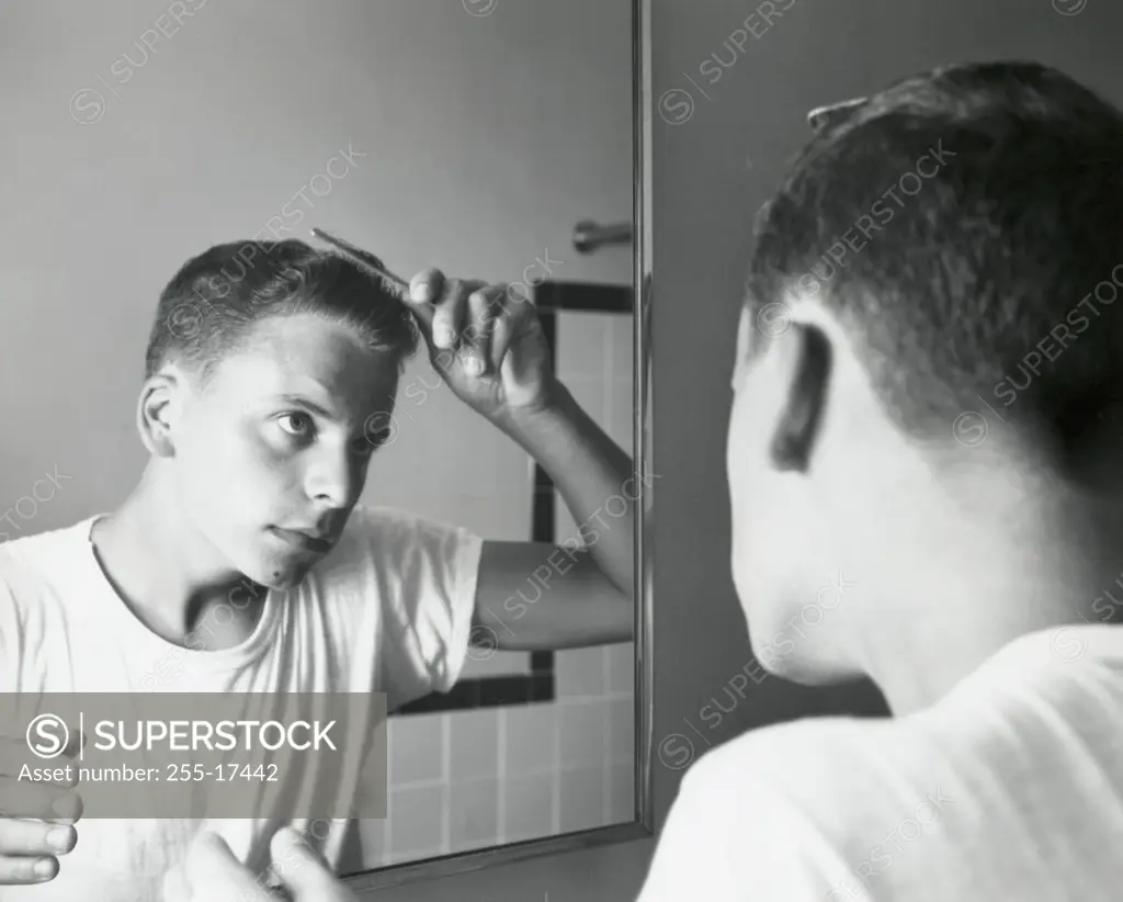Rear view of a teenage boy combing his hair in front of a mirror, 1960