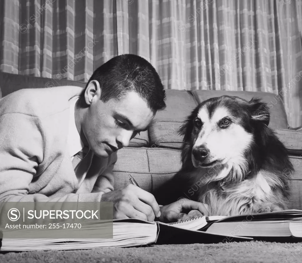 Teenage boy writing in a book and holding a paw of a dog