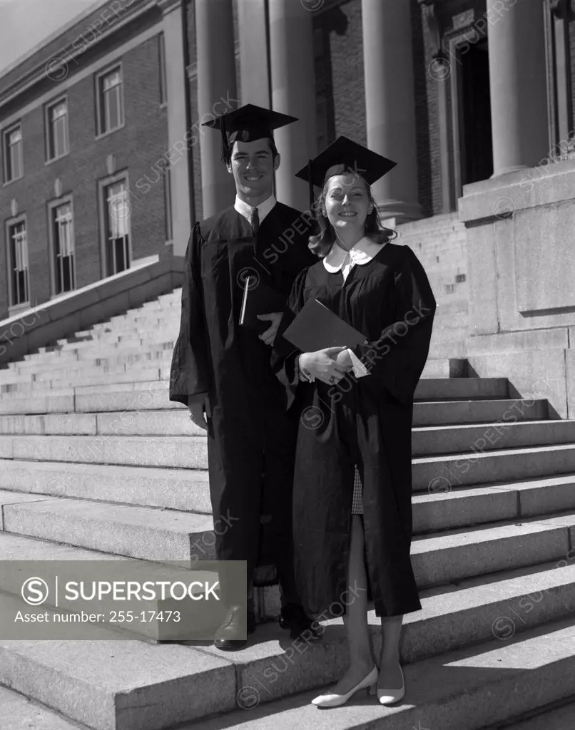 Portrait of a young couple dressed in graduation gowns smiling