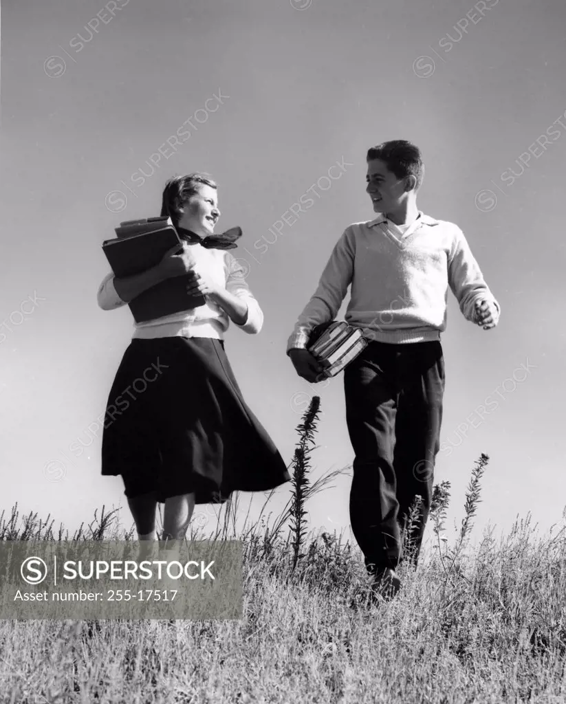 Teenage boy and teenage girl carrying books walking on meadow
