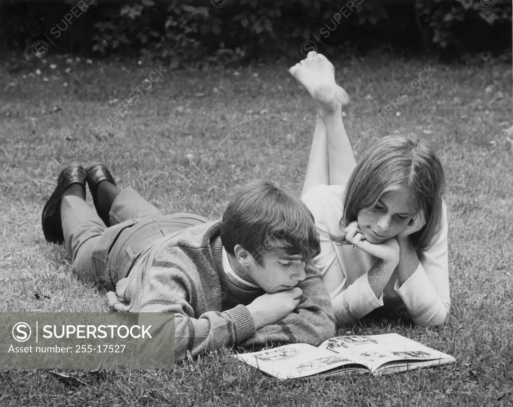 Teenage couple reading book in park