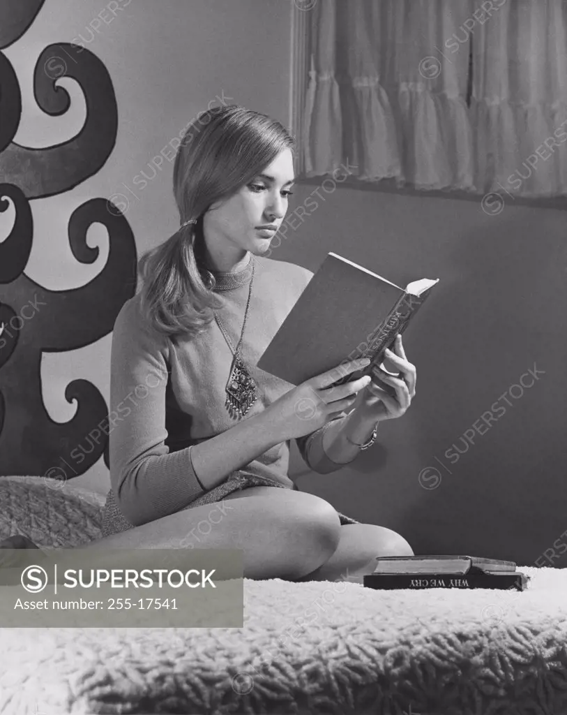 Teenage girl sitting on the bed and reading a book