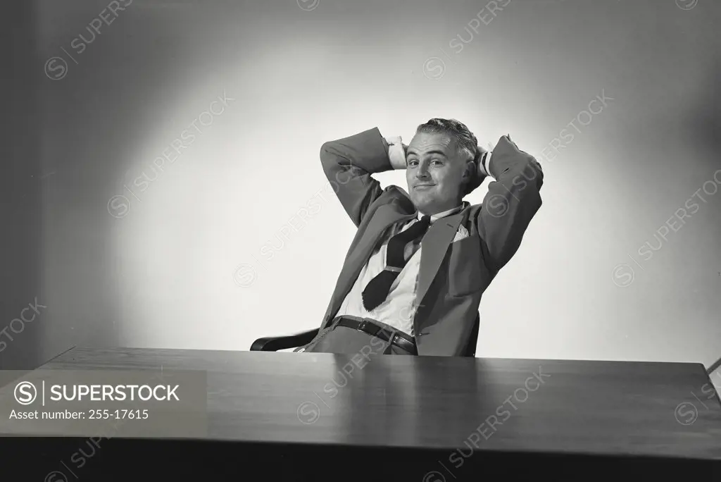 Businessman sitting at office desk relaxing with hands raised supporting his head