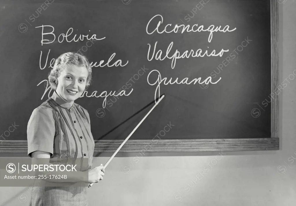 Vintage photograph. Portrait of a female teacher pointing to a blackboard in a classroom