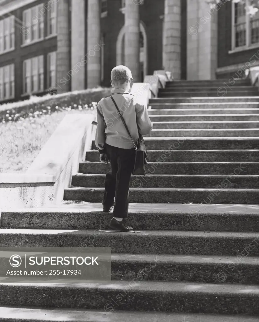 Rear view of a schoolboy climbing up a staircase to school