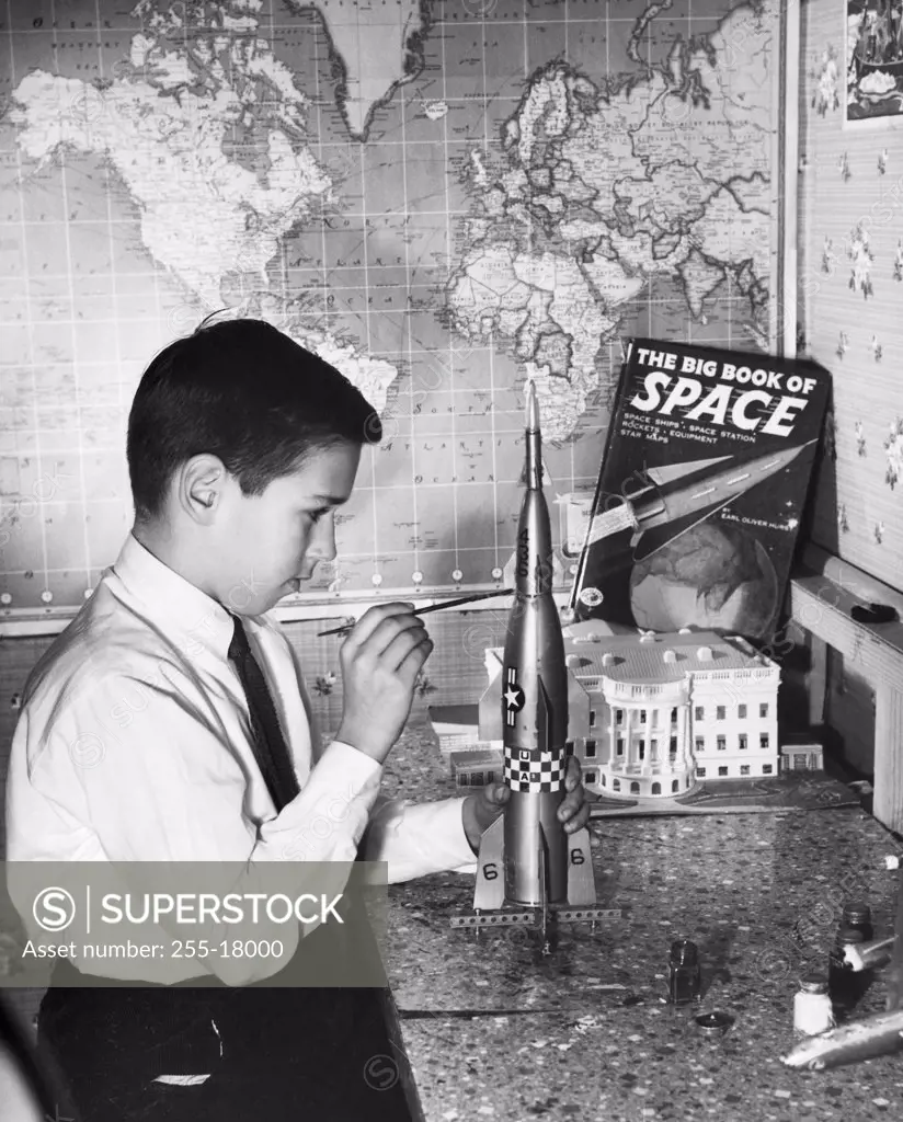 Side profile of a boy painting a model rocket