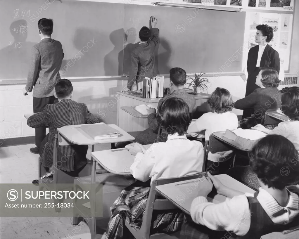 Rear view of two students writing on a blackboard in a classroom