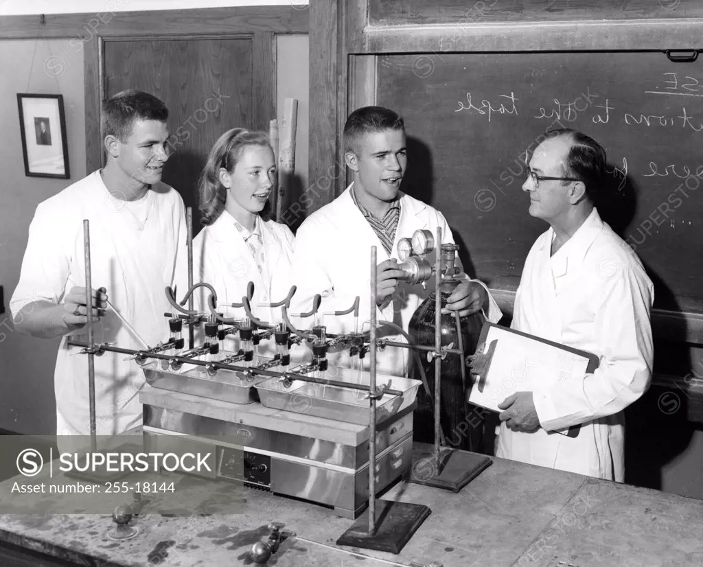 Three students standing with a teacher in a chemistry class