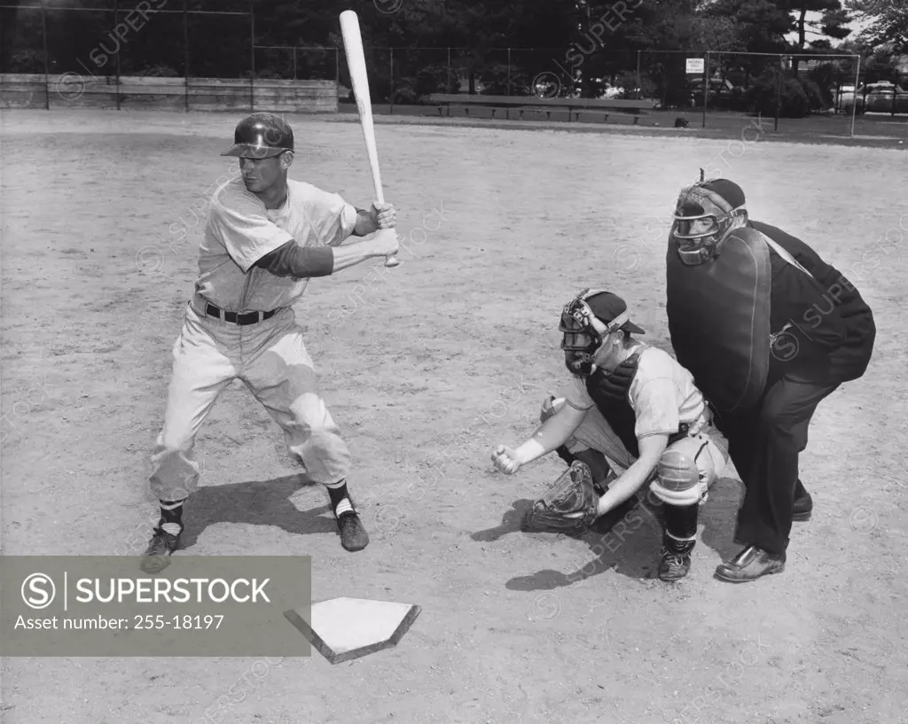 Baseball player swinging a baseball bat with a baseball catcher and a baseball umpire beside him