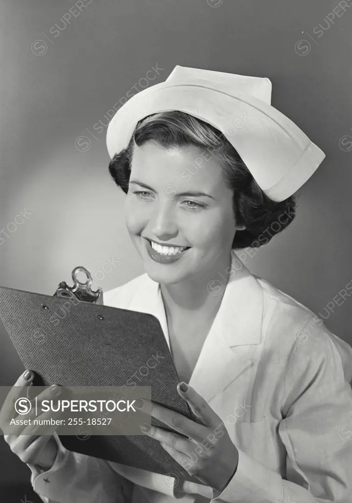Vintage photograph. Portrait of brunete woman in nurse uniform smiling looking at clipboard