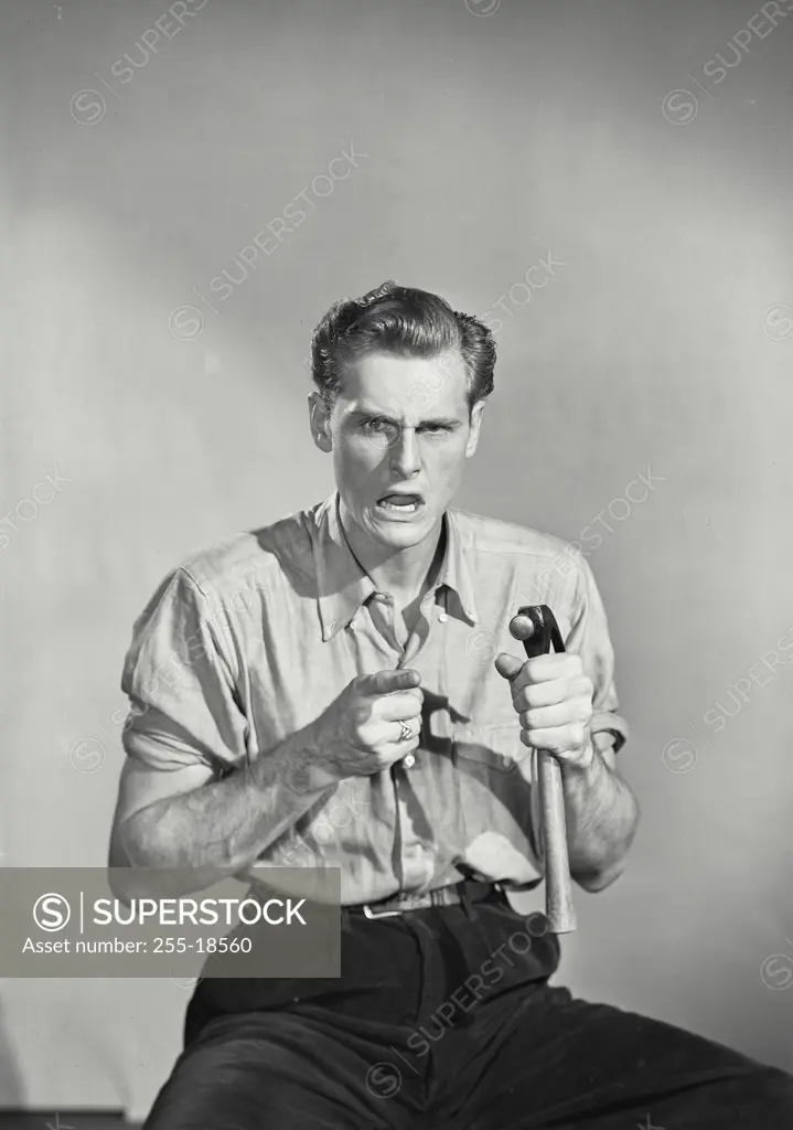 Vintage Photograph. Man in button shirt with angry face pointing and holding hammer