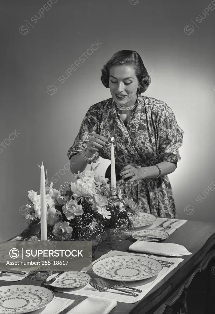 Vintage photograph. Woman lighting candles in centerpiece at dinner table.