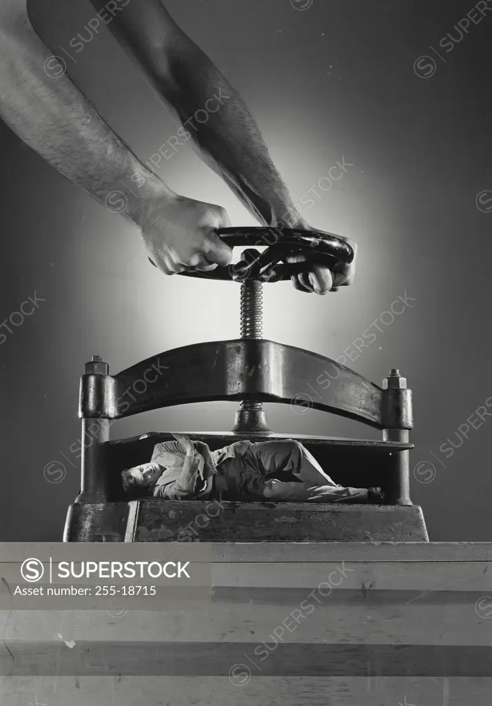 Vintage Photograph. Male hands turning wheel of cast iron book press squishing man laying in opening, composite photo