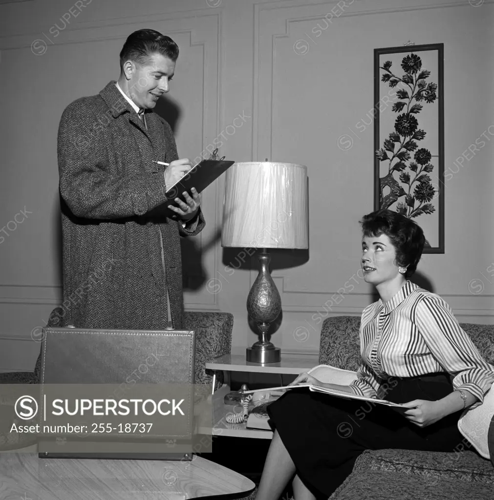 Insurance agent filling in form, while young woman is sitting on sofa holding open brochure
