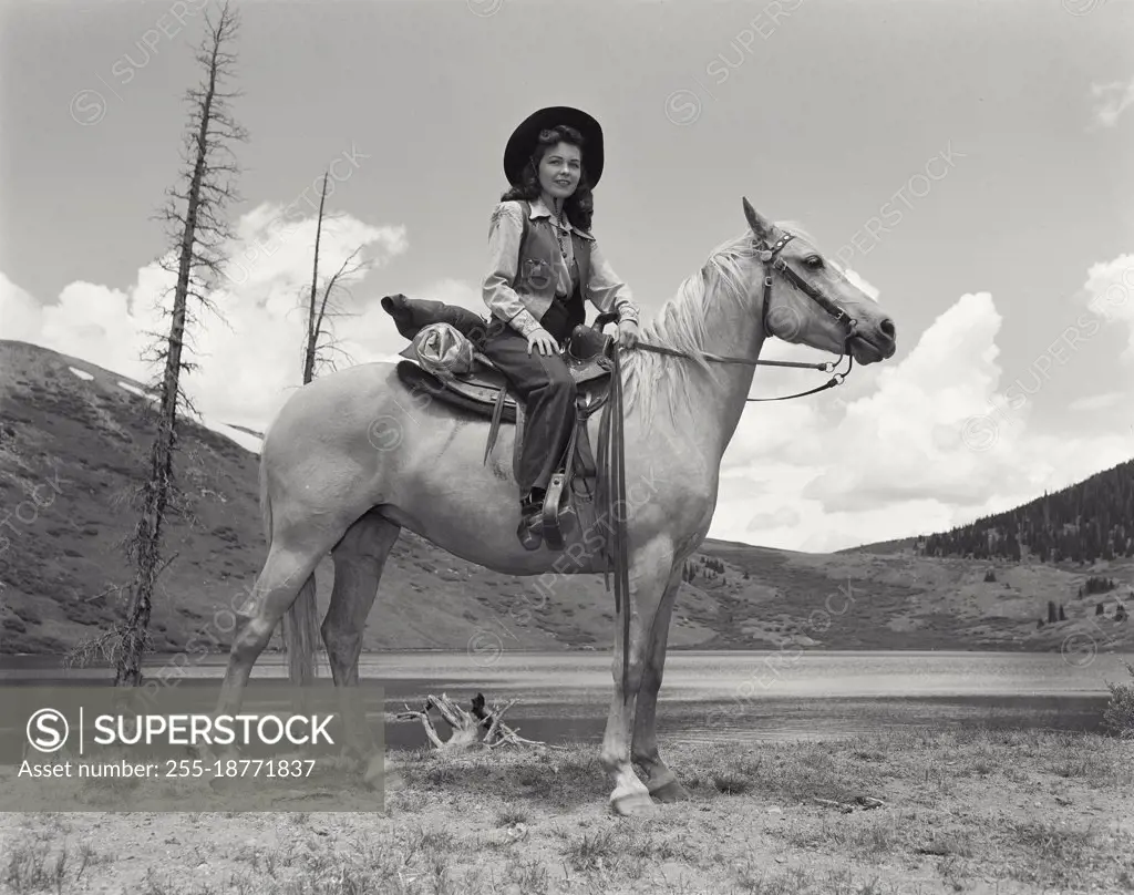 Vintage photograph. Woman sitting on horse in front of lake and mountains in Colorado. Model released