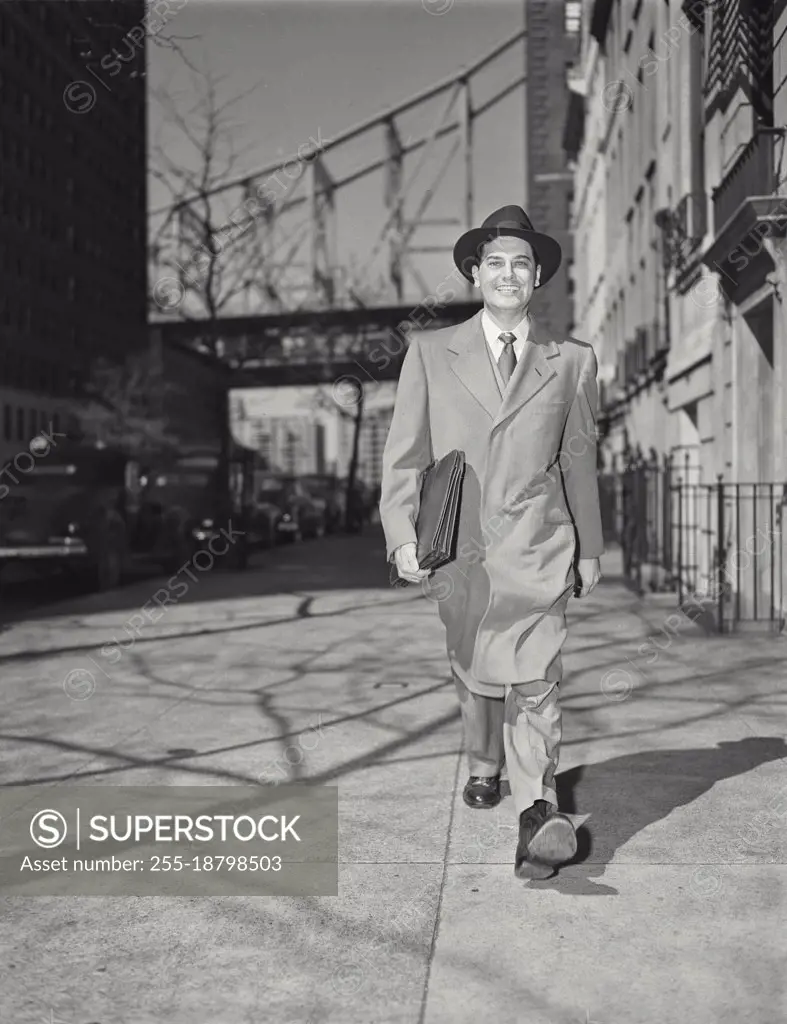 Vintage photograph. Businessman in long jacket and suit with briefcase walking on sidewalk. Model released.