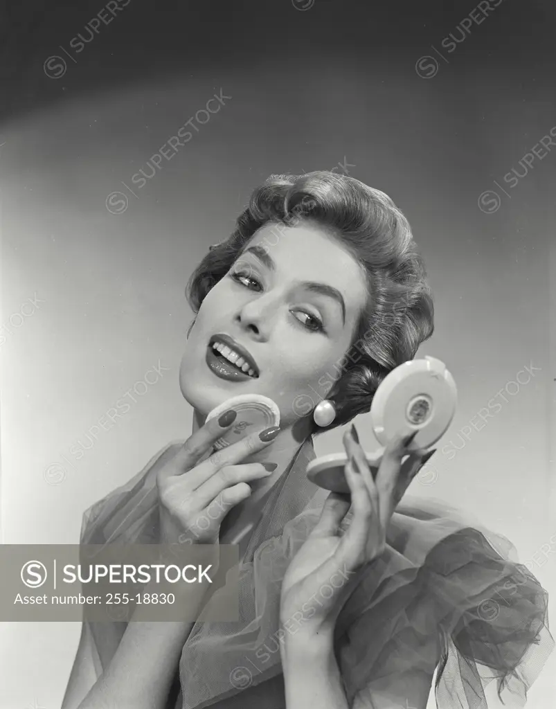 Vintage Photograph. Woman with short hairstyle smiling while putting on makeup, holding compact mirror