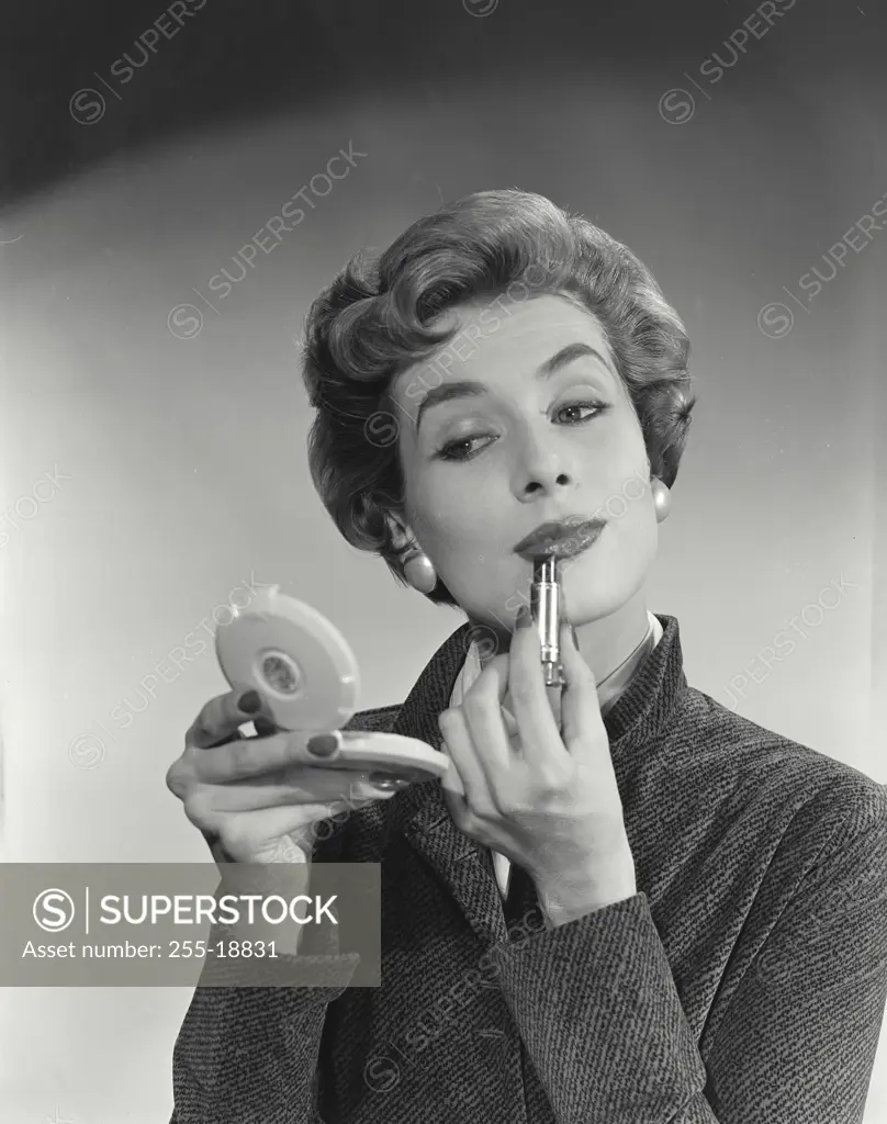 Vintage Photograph. Woman with short hairstyle putting on lipstick looking into compact mirror
