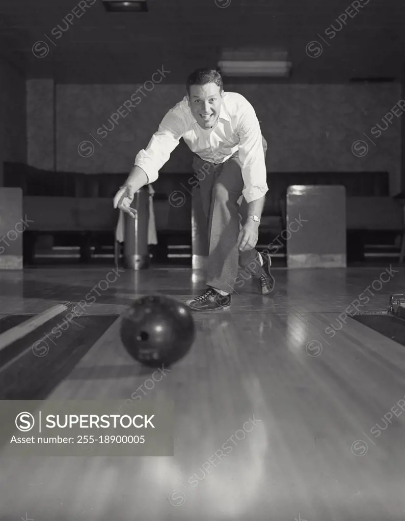 Vintage photograph. Man smiling throwing bowling ball down lane.