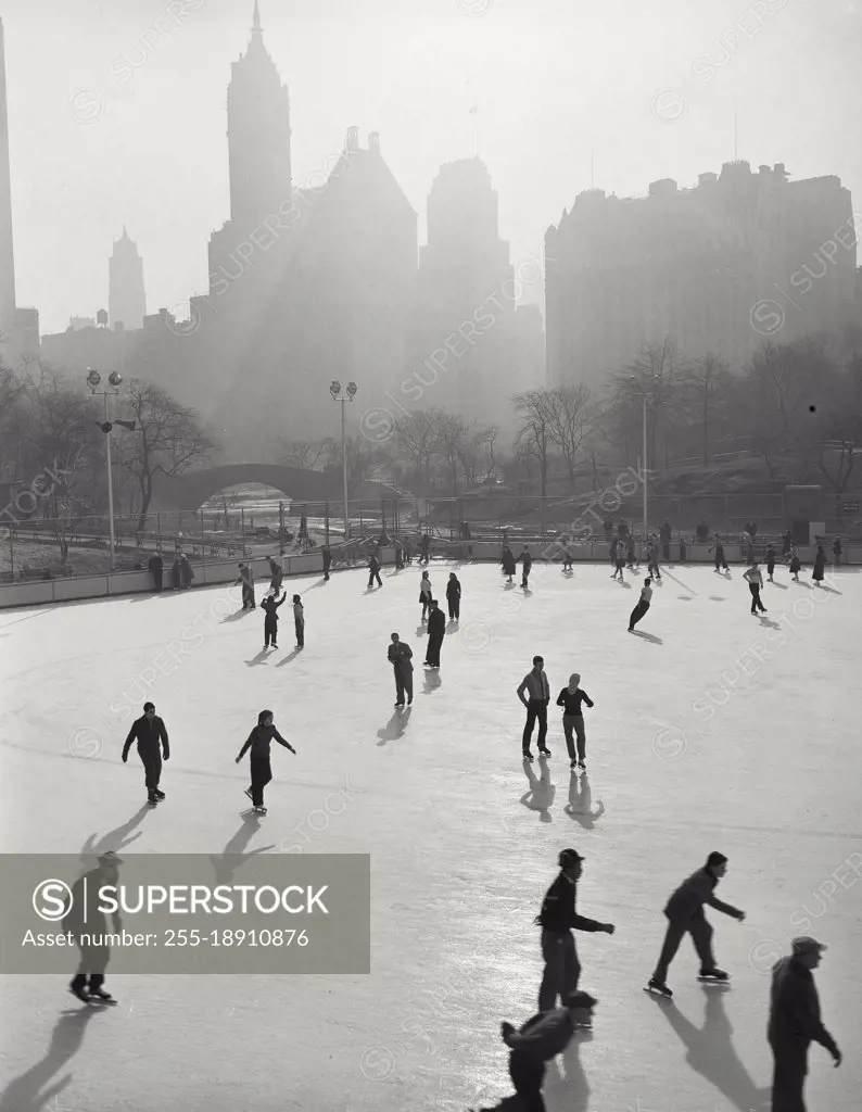 Vintage photograph. People skating at Wollman Memorial Ice Rink in Central Park with hazy buildings in background