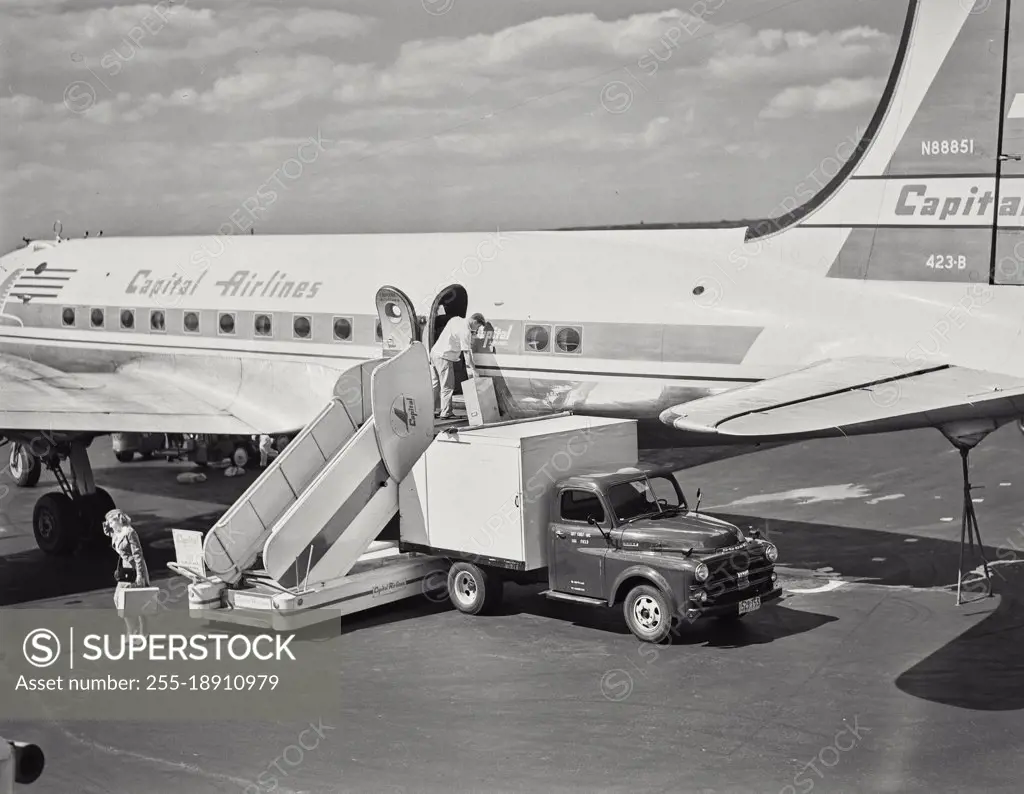 Vintage photograph. Man unloading luggage on stair car in front of Capital Airlines plane at La Guardia Airport