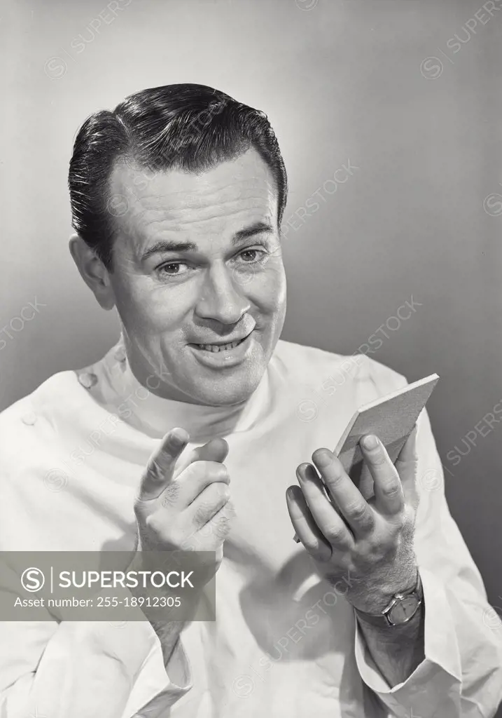 Vintage photograph. Man smiling wearing white surgeon smock holding notepad with raised hand and pointed finger