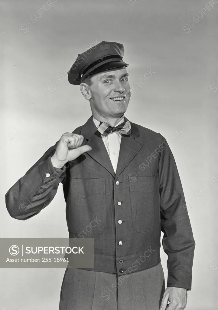 Vintage Photograph. Mailman in uniform wearing bow tie  pointing thumb at his chest smiling