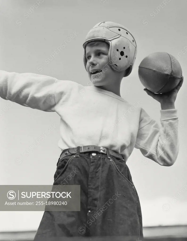 Vintage photograph. Young boy wearing football helmet turned to side with arm raised to throw ball