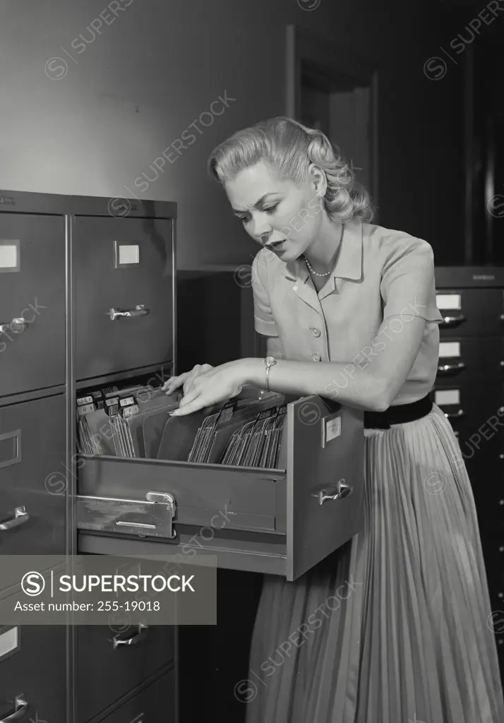 Vintage Photograph. Young woman wearing dress going through folders in drawer of filing cabinet, Frame 3