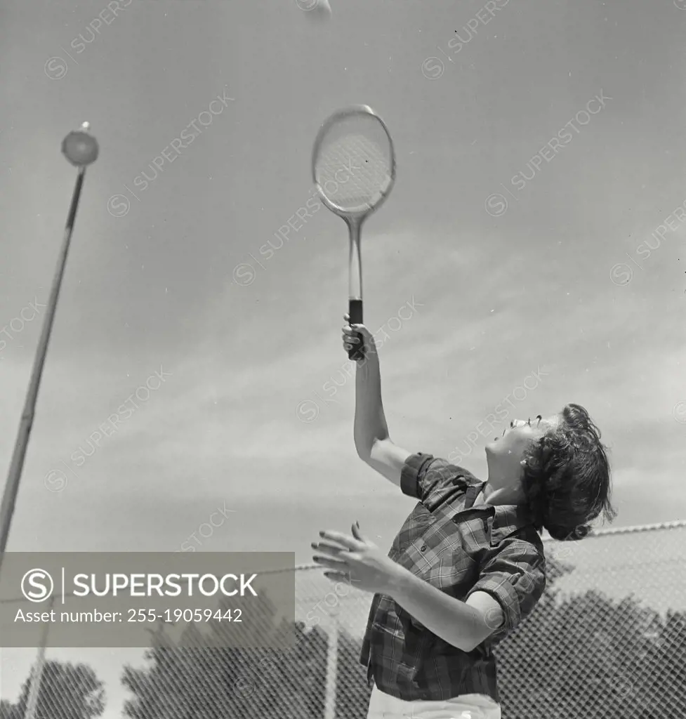 Vintage photograph. Young woman raising racket to serve tennis ball in mid air