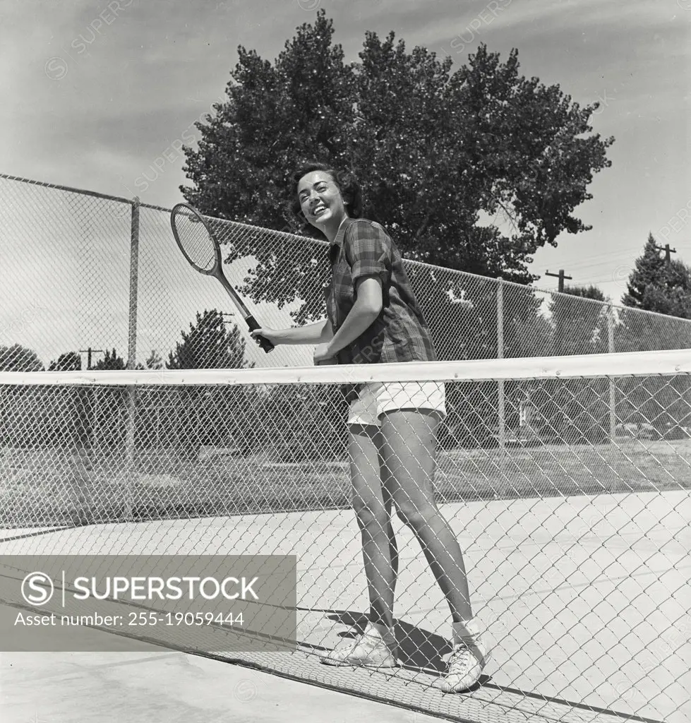 Vintage photograph. Young woman posing on tennis court behind net