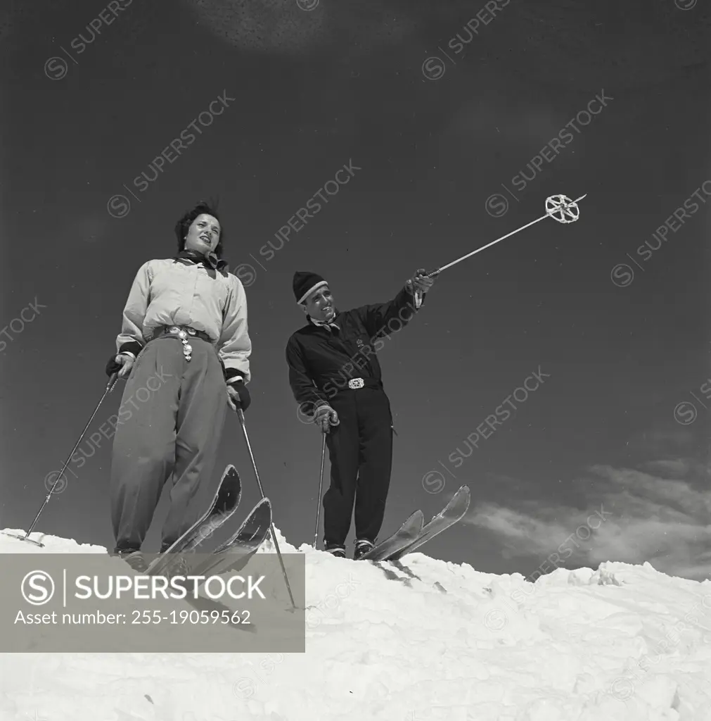 Vintage photograph. Ski couple in snow with man pointing with ski pole