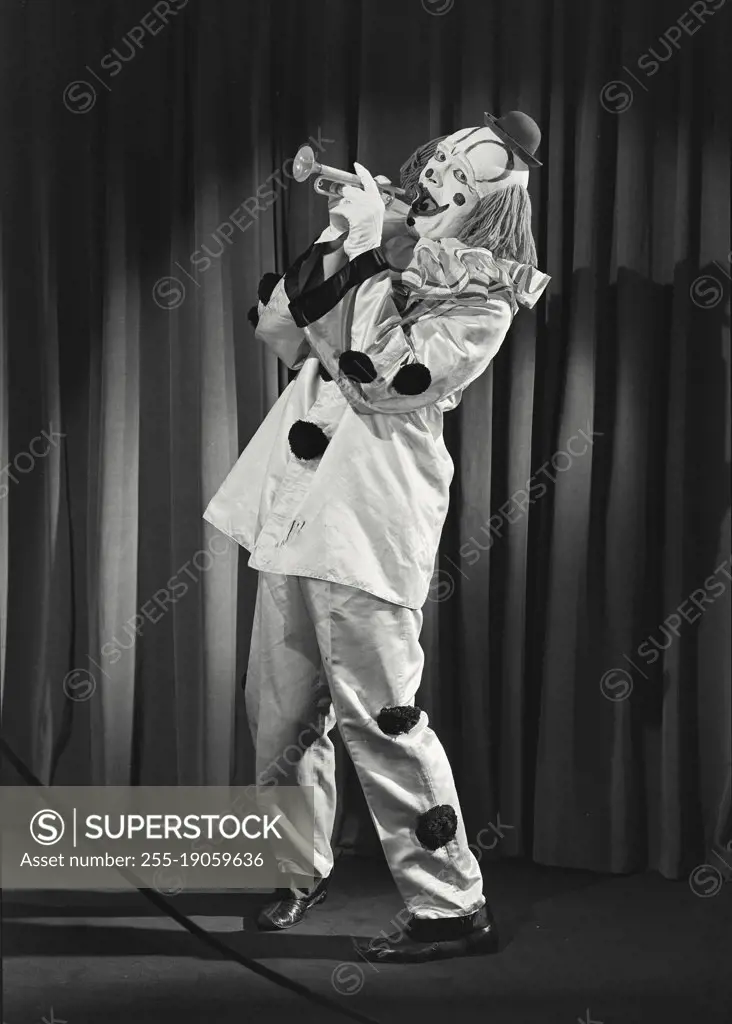 Vintage photograph. Portrait of clown wearing silly hat and playing toy horn