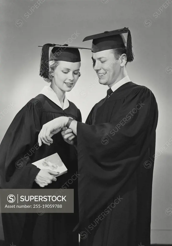 Vintage photograph. portrait of man and woman in cap and gown chatting about his watch