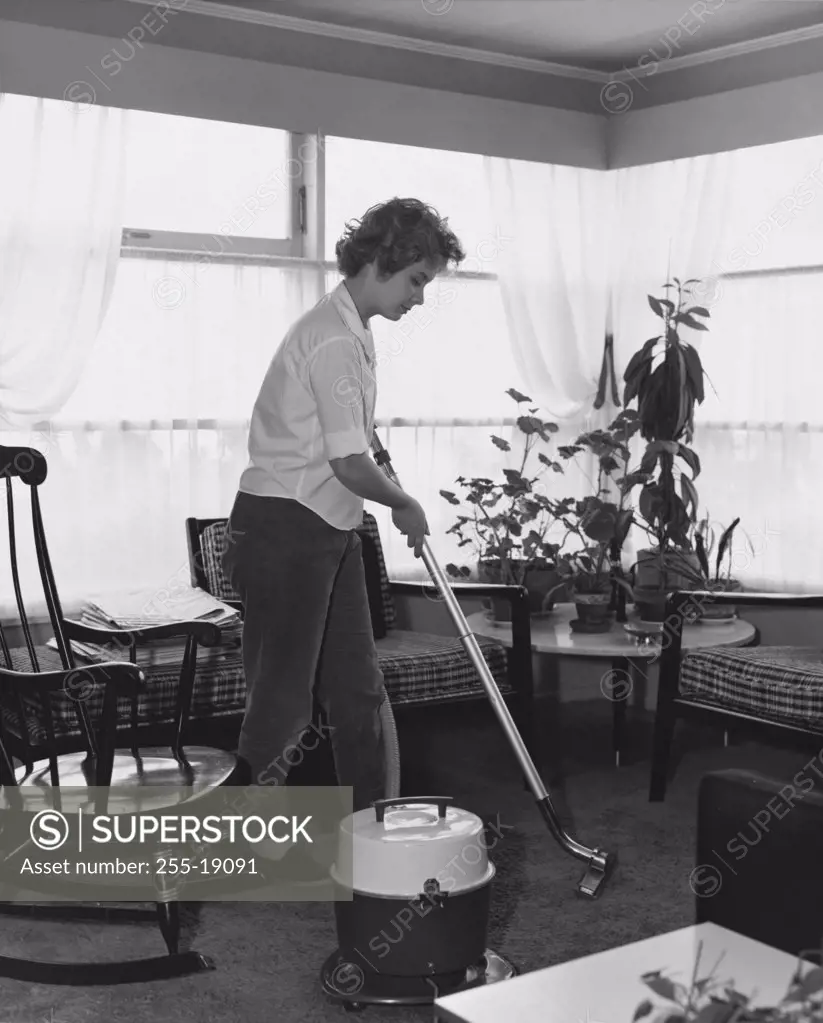 Side profile of a young woman cleaning a carpet with a vacuum cleaner