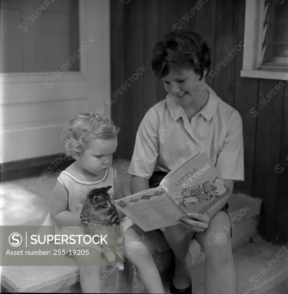 Mother with daughter sitting on porch reading book