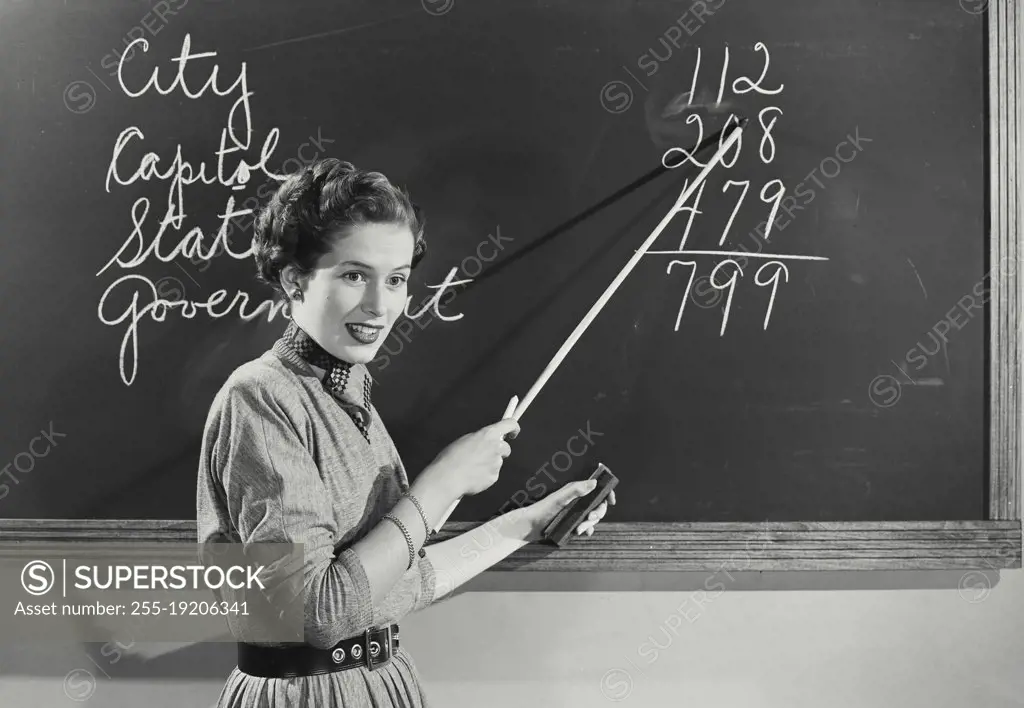 Vintage photograph. Teacher standing at chalkboard pointing to numbers