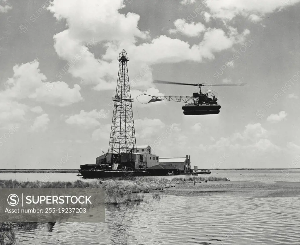 Vintage photograph. A Bell Aircraft Model 47D-1 helicopter comes in for a landing beside an oil well in the Louisiana marshes