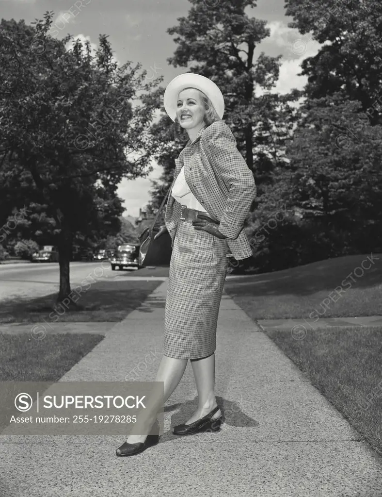 Vintage photograph. Woman in matching skirt and jacket on sidewalk smiling