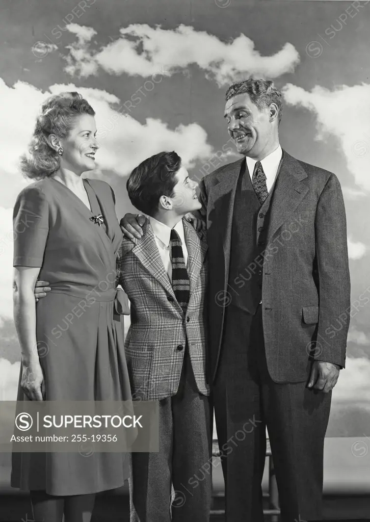 Vintage Photograph. Dressed up family of Father, Mother, and son smiling and standing close together in front of cloud sky background