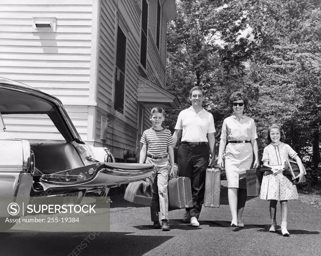 Family carrying luggage towards a car