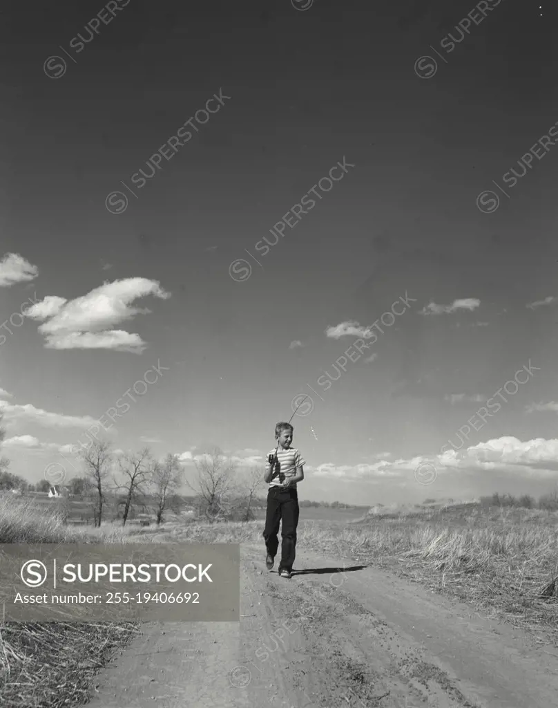 Vintage photograph. Boy walking down country road with fishing pole