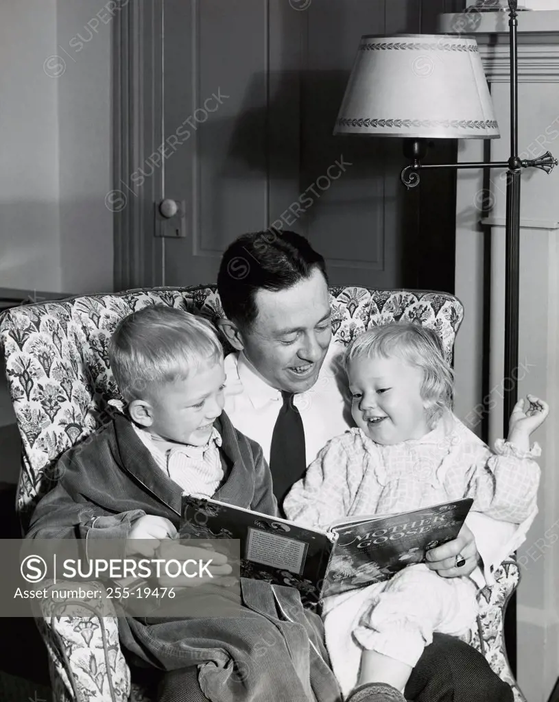 Close-up of a father sitting with his son and daughter reading a story book